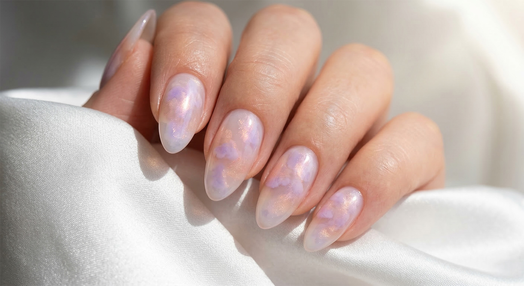 Marzycielski manicure w stylu cloud nails wiosna. Półprzezroczysta, mleczna baza z lawendowo-brzoskwiniową poświatą tworzącą subtelny efekt glow na paznokciach  w kształcie migdałka.