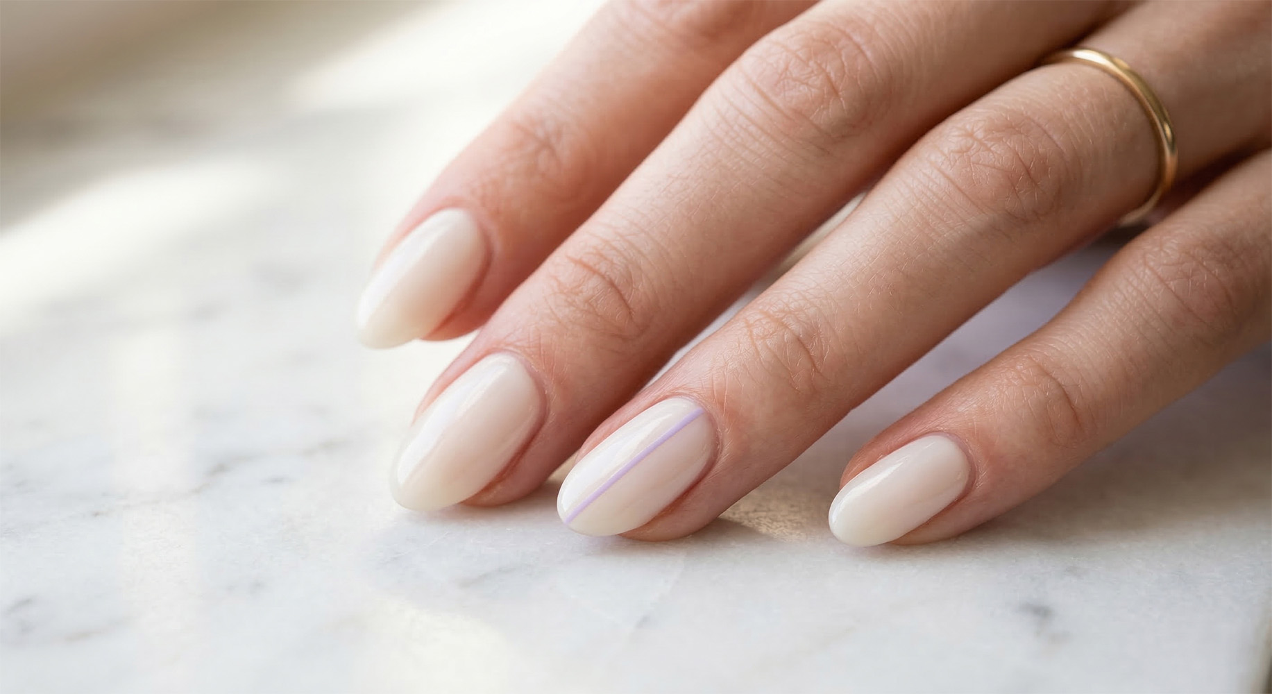 Elegancki manicure świąteczny na Wielkanoc. Owalne paznokcie nude na święta wielkanocne w ciepłym, mlecznym odcieniu z bardzo subtelną, lawendową linią. Minimalistyczna stylizacja z lśniącym wykończeniem.