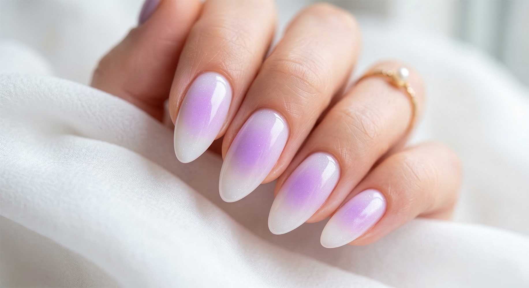 Lawendowe paznokcie wielkanocne 2026 z wiosennym efektem rozmycia. Płynne przejście od lawendowego środka do mlecznej bieli na brzegach paznokci opiłowanych w kształt migdałka z lśniącym wykończeniem.