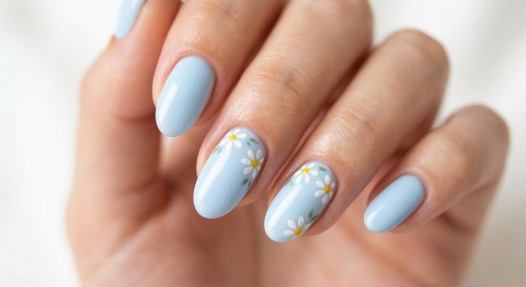 Paznokcie wielkanocne baby blue 2026 z ręcznie malowanymi stokrotkami. Wiosenny manicure na owalnych paznokciach z motywem kwiatowym, oświetlony naturalnym światłem.